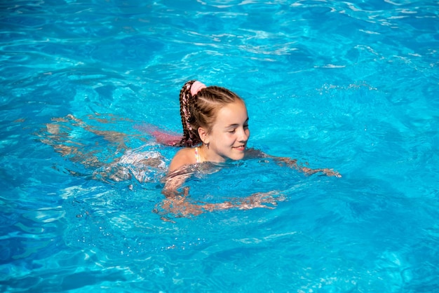 A teenage girl swims in a pool with blue water She has african braids braided with zizi ribbons