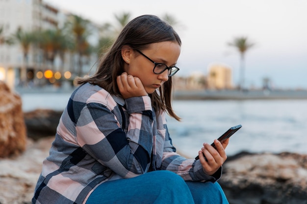 A teenage girl talks on the phone against the backdrop of city
and the sea on a hot evening