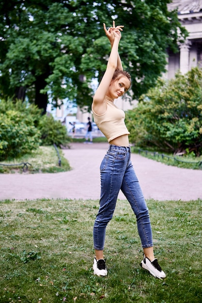 Teenage girl in tank top and jeans stretches in city park