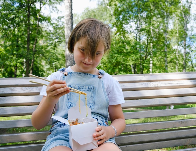 A teenage girl on a walk on a summer day in the park has lunch with noodles wok