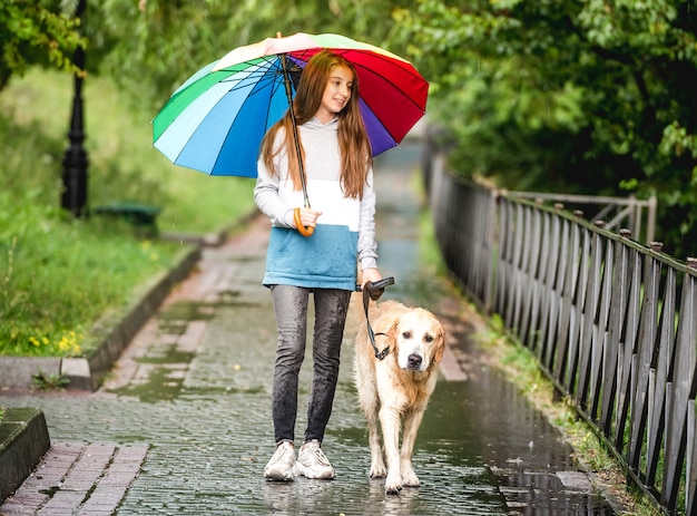 Teenage girl walking with golden retriever dog at rainy day