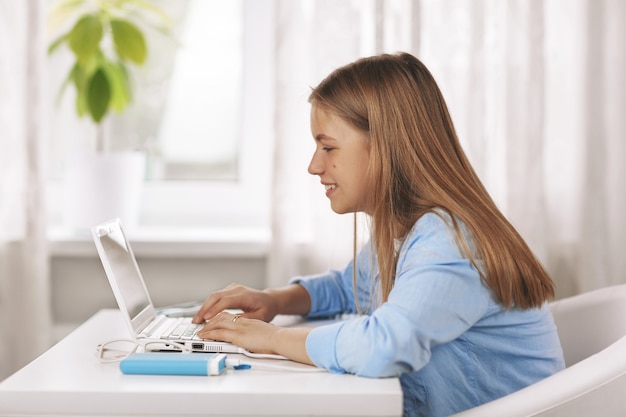 Teenage girl wearing headphones sitting at table and doing homework