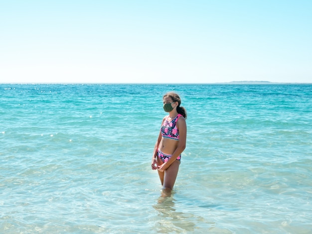 Teenage girl wearing a protective mask on the beach to prevent coronavirus disease