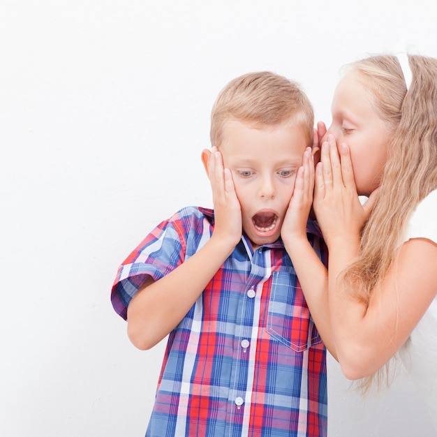 Teenage girl whispering in the ear of a secret teen boys on white background