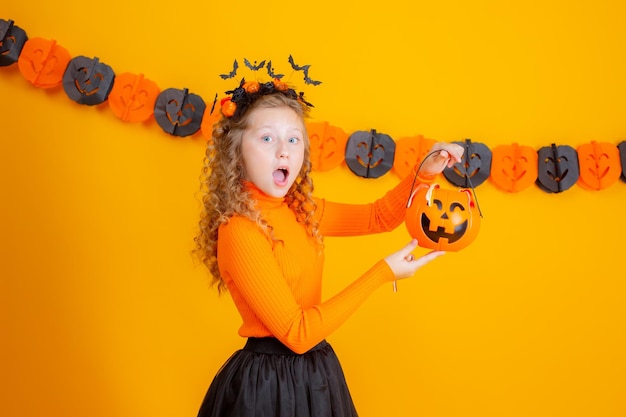 teenage girl witch costume on yellow background holding confent pumpkin marmalade worms halloween