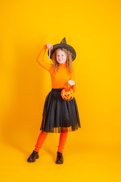 teenage girl witch costume on yellow background holding confent pumpkin marmalade worms halloween