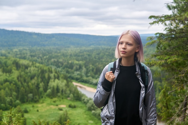 Фото Девочка-подросток с рюкзаком идет по вершине горы на фоне лесистых холмов и реки