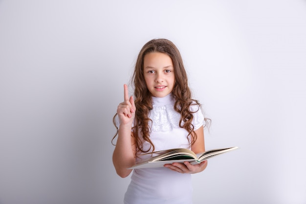 Фото Девочка-подросток с книгой в ее руках на белой предпосылке. показывает эмоции радости, удивления, грусти.