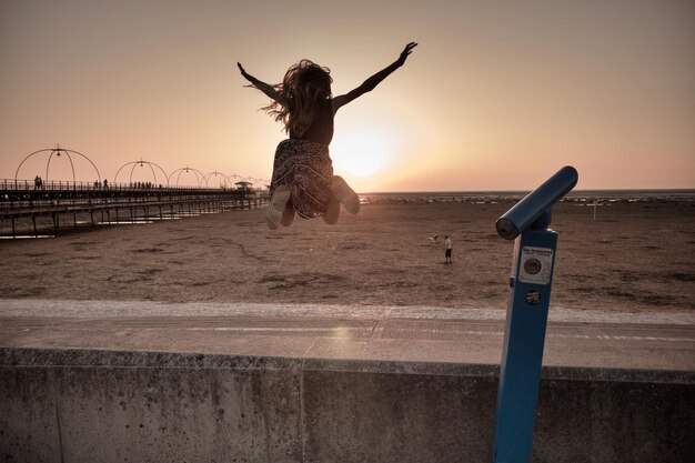 Foto ragazza adolescente con le braccia tese che salta sulla spiaggia contro il cielo durante il tramonto