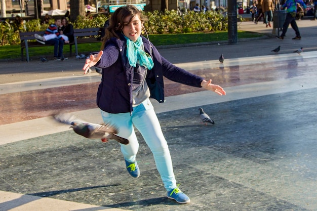 Teenage girl with arms outstretched while chasing pigeon on footpath