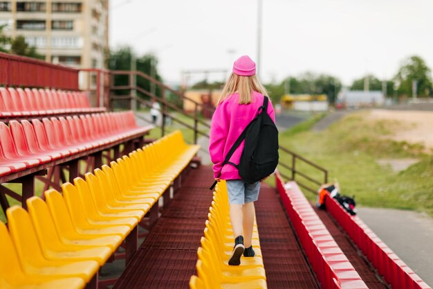 A teenage girl with a backpack walks through the stands of the school stadium rear view