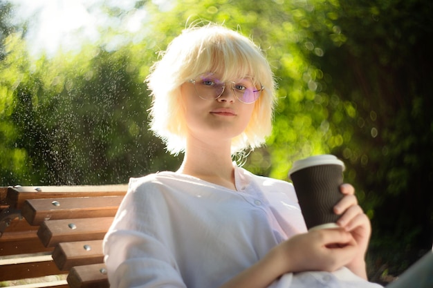 Teenage girl with blond hear drinking coffee from craft paper cup outside