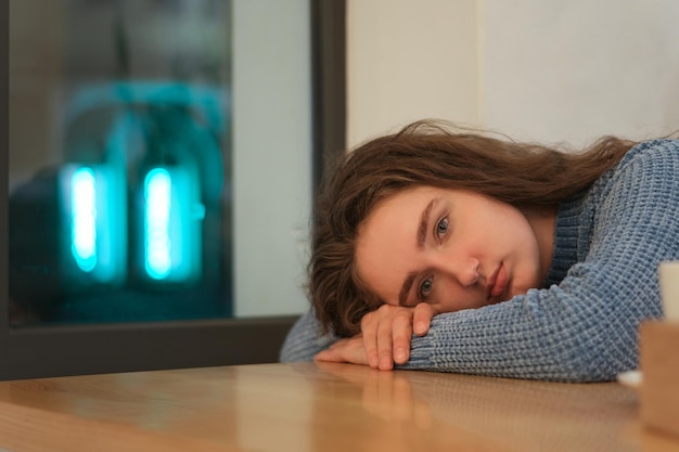 Teenage girl with brown hair put head on table Sad young woman lies on table inside cafe