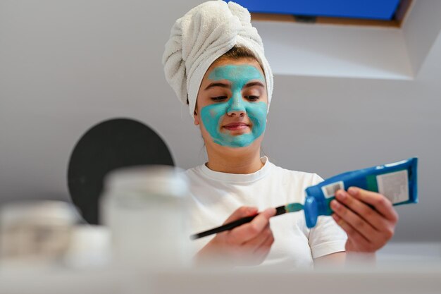 Teenage girl with brush applying clay mask to face