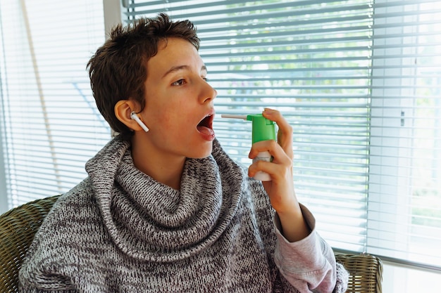 Photo teenage girl with cough treats throat with medicinal spray.