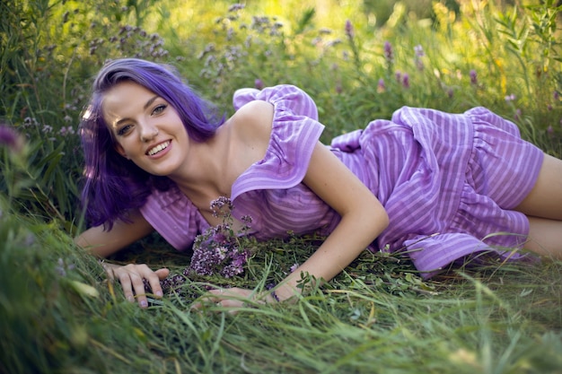 Teenage girl with dyed purple hair and a nose piercing in the grass with a bouquet of flowers and in a short dress