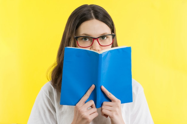 Девочка-подросток в очках смотрит на книгу