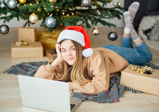 Teenage girl with gifts and laptop near the Christmas tree. Living room interior with Christmas tree and decorations. New Year. Gift giving.