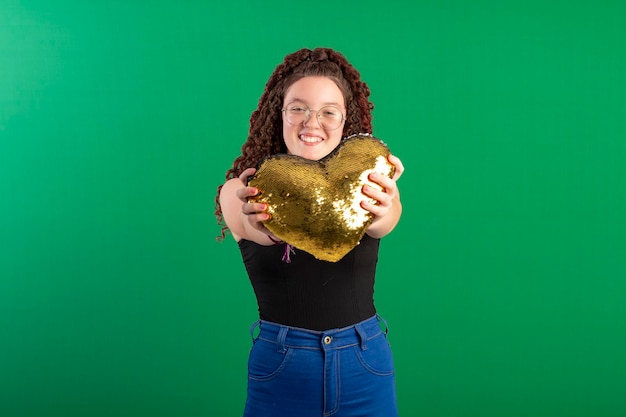 Teenage girl with glasses holding a shiny heart in fun poses in studio photo with green background ideal for cropping