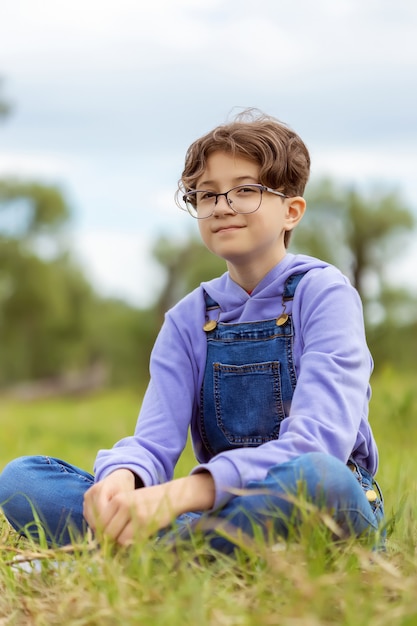 teenage girl with glasses sits on green meadow