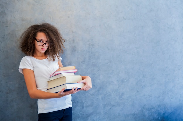 Teenage girl with glasses stands next to the wall and holds several books