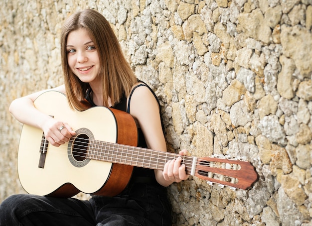 Teenage girl with a guitar against a brown wall