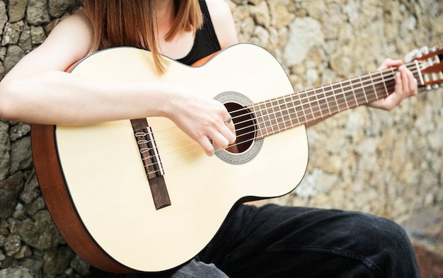 Teenage girl with a guitar against a brown wall