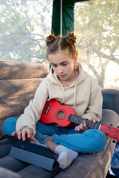 A teenage girl with a little guitar ukulele communicates online on the gadget Online learning