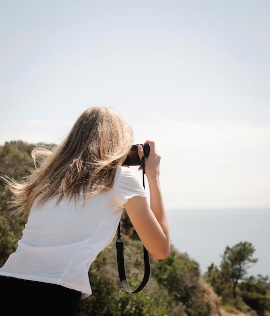 Foto adolescente con lunghi capelli biondi che guarda attraverso una macchina fotografica, scatta una foto.