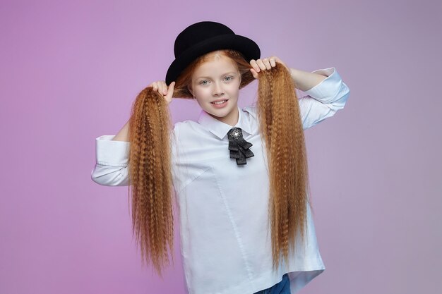 Teenage girl with long red hair and a hat. photo session in the studio on a pink background