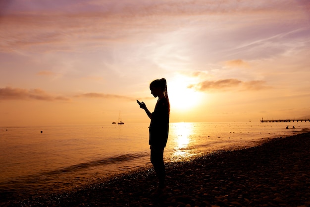 Una ragazza adolescente con un telefono sullo sfondo del mare al tramonto riposo comunicazione online estate