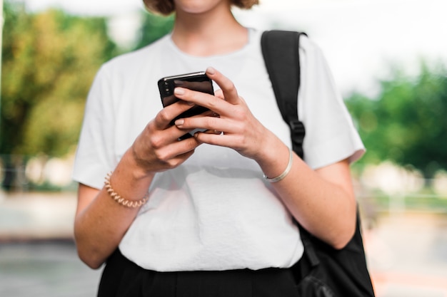 Девочка-подросток со школьным рюкзаком и телефоном в кампусе после учебы с помощью телефона