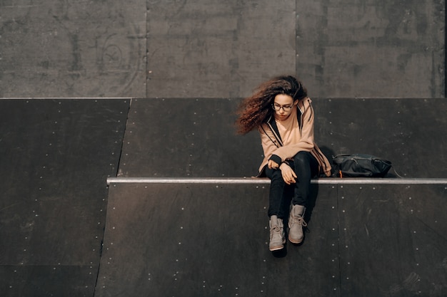 Photo teenage girl with serious facial expression enjoying music and sitting in skate park