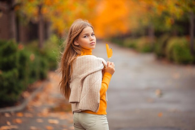 Photo a teenage girl in a yellow sweater walks along a street outside the city against the backdrop of yellow trees fun walk in autumn