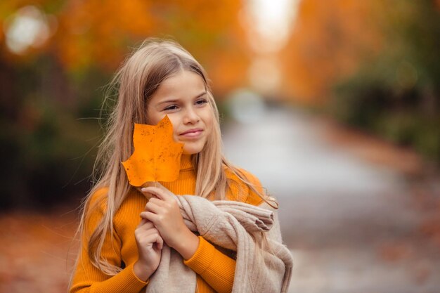 Photo a teenage girl in a yellow sweater walks along a street outside the city against the backdrop of yellow trees fun walk in autumn