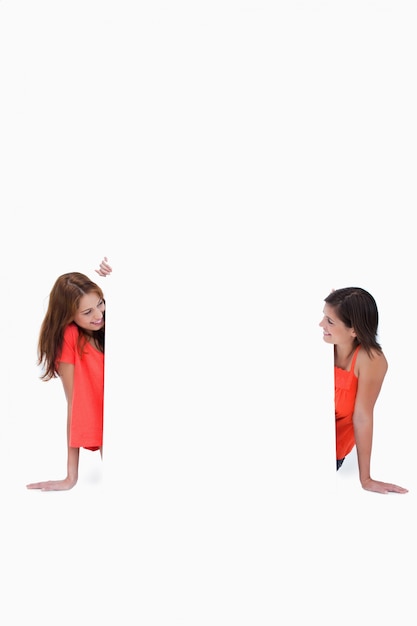 Photo teenage girls looking at each other in front of a blank poster