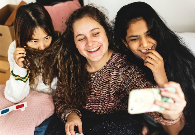 Teenage girls using a smartphone to take a selfie in a bedroom hangout and friendship concept