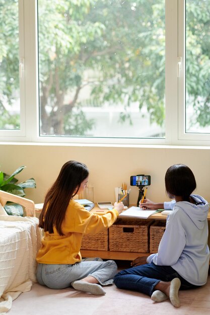 Teenage girls watching online lection on smartphone and writing\
in notepad