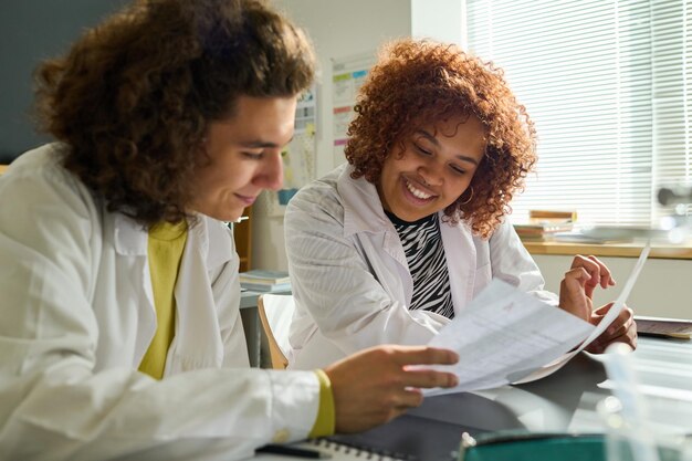 Adolescente che mostra carta con compiti di prova al compagno di classe afroamericano