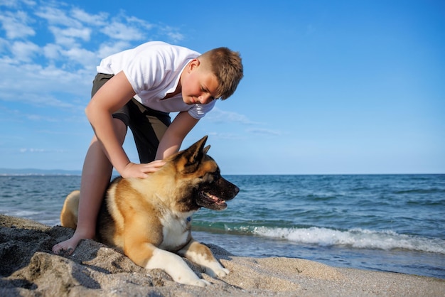 Ragazzo adolescente con capelli biondi e guinzaglio in mano gioca e cammina con il cane di razza akina inu sulla spiaggia selvaggia lungo il mar nero