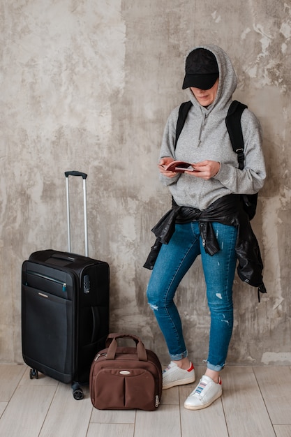 Teenage hipster girl with suitcases on the background of a concrete wall in the waiting room of transport.