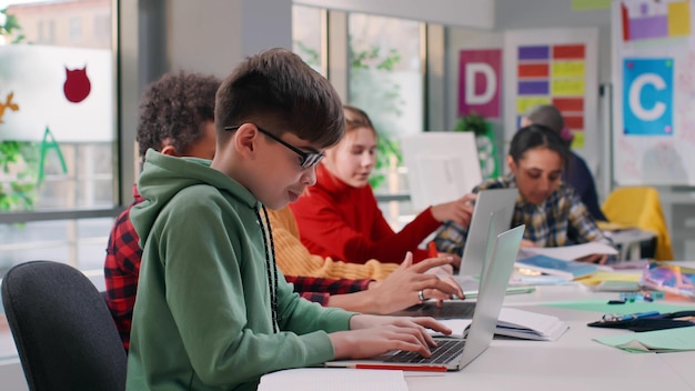 10대 남학생이 책상에 앉아 노트북을 사용하여 노트북에 작업을 작성합니다.