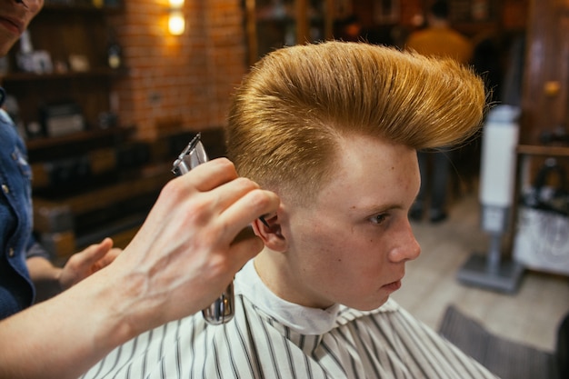 Parrucchiere adolescente di tagli di capelli del ragazzo di redhead nel negozio di barbiere. acconciatura retrò alla moda alla moda