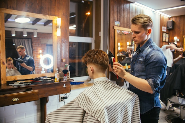 Parrucchiere adolescente di tagli di capelli del ragazzo di redhead nel negozio di barbiere. alla moda