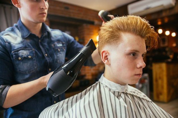 Parrucchiere adolescente di tagli di capelli del ragazzo di redhead nel negozio di barbiere