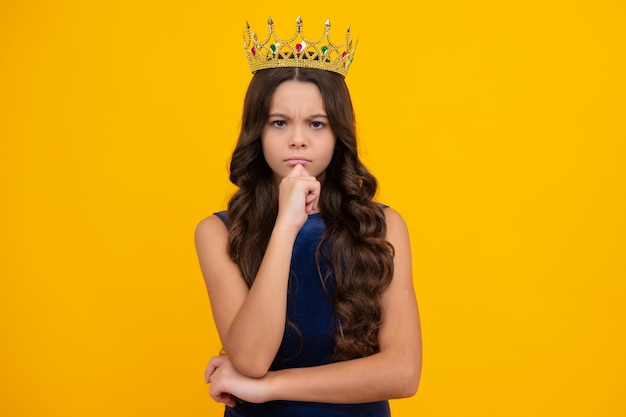 Teenage selfish girl celebrates success victory Teen child in queen crown isolated on yellow background Princess in tiara Prom party Thinking face thoughtful emotions of teenager girl