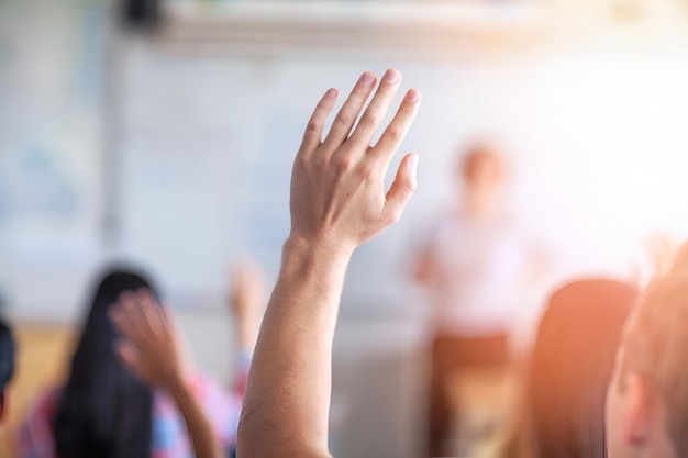 teenage student asking while raising hand in illuminated classroom
