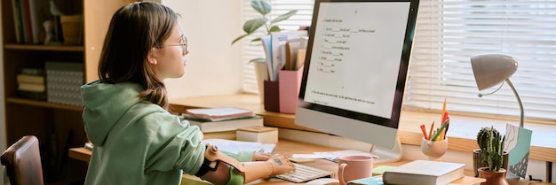 Teenage student engaged in coursework at organized desk with healthy plant and computer screen