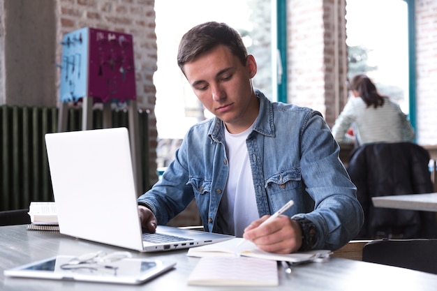 Teenage student sitting at table with notebook and writing