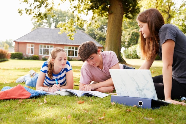 Teenage Students Sitting Outdoors And Working On Project